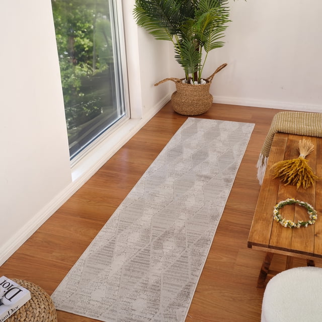 Rug Branch Astra Modern Indoor Area Rug, Grey, abstract geometric runner rug with 0.4-inch pile height on wooden floor near a large window. Made of polyester with jute backing, it suits high-traffic indoor areas like hallways and entryways. The rug is shown in a bright room with a woven basket plant and wooden bench with a yellow throw and floral wreath.