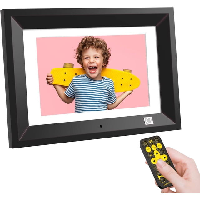 KODAK 10.1 Inch Wood Digital Picture Frame with Remote Control displaying a photo of a child holding a yellow skateboard on a pink background, with a black frame featuring the Kodak logo and a hand holding the remote control with yellow buttons, ideal for easy slideshow viewing and programmable auto on/off.