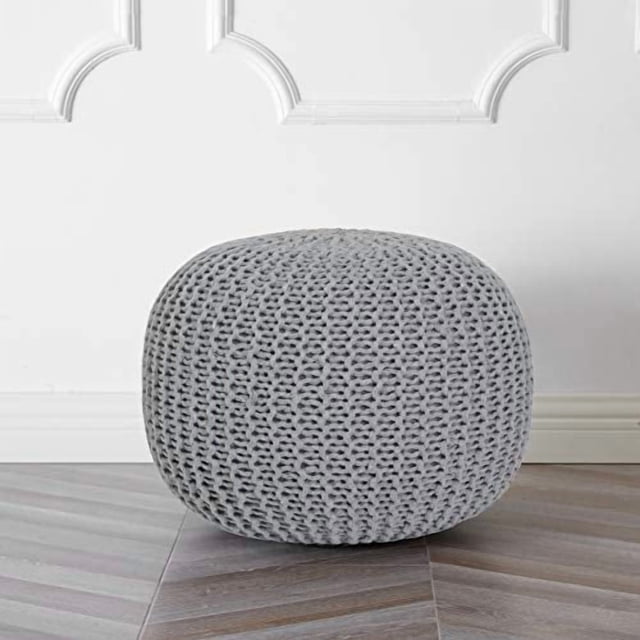 Urban Shop Pouf Rond en Tricot Gris Pâle, avec un design en Coton Texturé Cousu à la Main et une surface en polyester Tricoté Doux. le Pouf Mesure 18 Pouces de Diamètre et 15 Pouces de Hauteur, Ce Qui en Fait un Ajout Polyvalent aux Salons, Chambres Ou Pouponnières. Il Est Rempli de Billes de Mousse Légères pour le Confort et une Portabilité Facile, Supporte jusqu'à 225 Lb. Présenté dans un Décor Intérieur avec un Plancher Ton Neutre et un Panneau Mural Blanc.