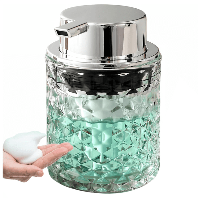 Foaming Hand Soap Dispenser, a refillable clear glass dispenser with an engraved textured design and a silver pump top. Suitable for dispensing foam soap, lotion, or dish soap, it is ideal for bathroom or kitchen countertop use. Shown dispensing rich foam soap into a hand.