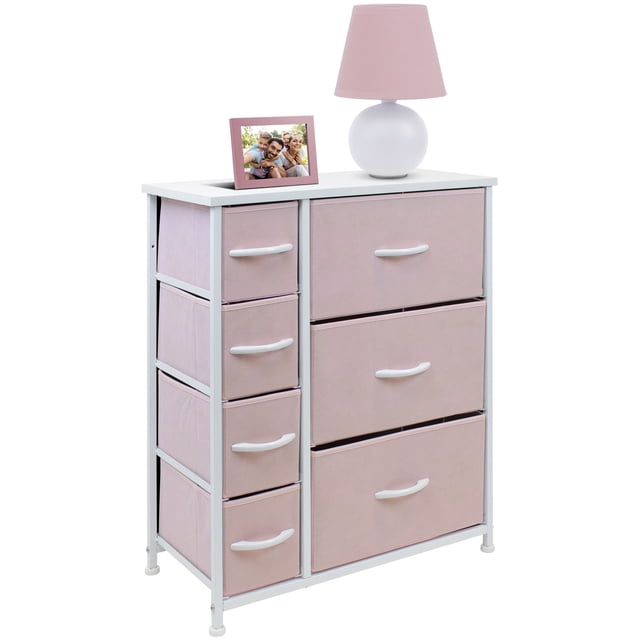 7 Drawers Chest Dresser - Pink by Sorbus, featuring a white steel frame with a smooth MDF wood top and seven pastel pink fabric drawers. The dresser includes a mix of small and large pull-out drawers with white handles, ideal for storing kids' clothes, toys, and linens. The top surface is styled with a pink lamp and a photo frame, showcasing its use for display. Measures approximately 25” L x 11.87” W x 28.75” H.