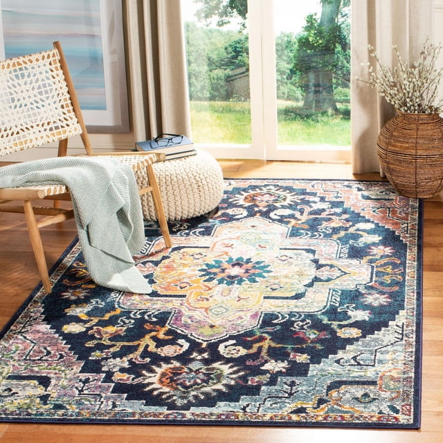 SAFAVIEH Crystal Debra Floral Area Rug with close cut pile and intricate floral medallion patterns in navy, cream, orange, and pink, power loomed from synthetic yarns, placed on hardwood floor in a sunlit room with woven chair, knitted pouf, and large window, ideal for transitional living or dining rooms.