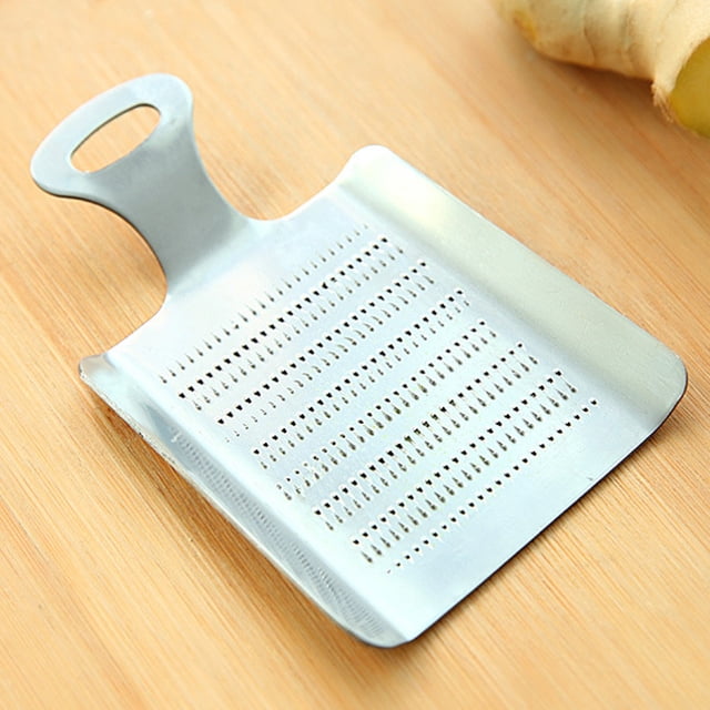Graters for Kitchen Stainless Steel Practical Kitchen Ginger Wasabi Stainless Steel Garlic Grater Bento Mill Tool. A compact, rectangular stainless steel grater with fine perforations designed for precise grinding of garlic, ginger, and wasabi. Features an ergonomic handle for easy grip and a flat base for stability. Approximate dimensions are 11.1 x 7.1 cm (4.37 x 2.8 inches). Shown on a wooden surface with a piece of ginger nearby.