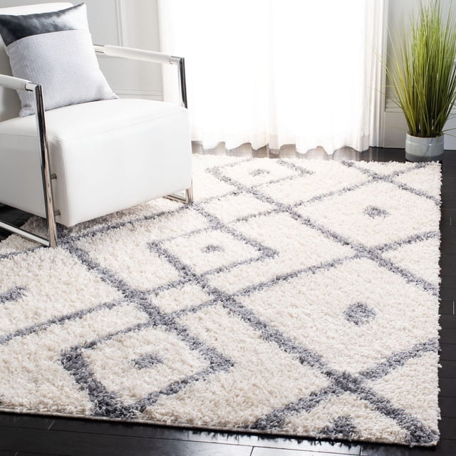 Safavieh Venus Tapis Shag Abstrait Avaline Présentant une Peluche de 1,77 Po à Poil Moyen en Fil Synthétique Blanc avec des Motifs Géométriques de Carrés Gris, Exposé sur des Planchers de Bois Franc Sombres à Côté d'Un Fauteuil Moderne Blanc et d'Une Plante en Pot Verte dans une Pièce Lumineuse, Idéal pour Ajouter une texture Chaude et un Intérêt Visuel à une Déco Contemporaine Ou Campagnarde Chic.