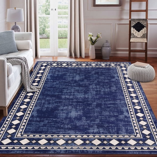 Garvee 5'x7' geometric bordered area rug in blue displayed in a contemporary living room setting. This washable area rug features a low-pile design with a soft texture and stain-resistant polyester material. Its geometric border pattern adds a stylish touch, complementing the surrounding decor. The rug includes a non-slip backing for safety and is machine washable for easy maintenance, making it ideal for living rooms, bedrooms, or dining rooms.