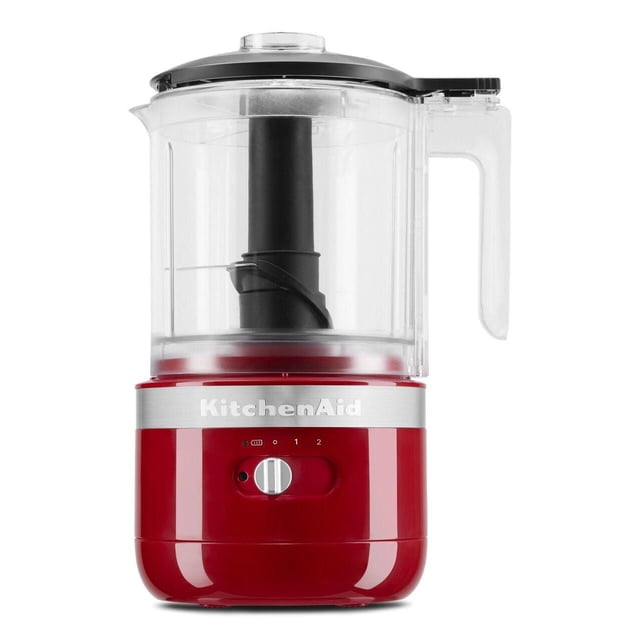 KitchenAid® 5 Cup Cordless Food Chopper in red with clear 5-cup BPA-free bowl, black stainless steel blade, silver control dial with two speed settings, and silver KitchenAid logo band, shown front-facing on white background, ideal for chopping and pureeing ingredients.