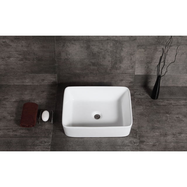 A&E Bath and Shower MIA Évier, un Évier Rectangulaire en Céramique de Chine Blanche à Vitreux avec Coins Arrondis et drain central, Monté au-Dessus du Comptoir sur des Carreaux Gris Foncé, avec une Serviette Brune Roulée et du Savon Blanc sur une Coupelle Transparente à Gauche, et un vase Noir avec des Brindilles à Droite, Présentant une surface Polie Résistante aux Taches et aux Égratignures Adaptée à la Rénovation de Salle de Bain.
