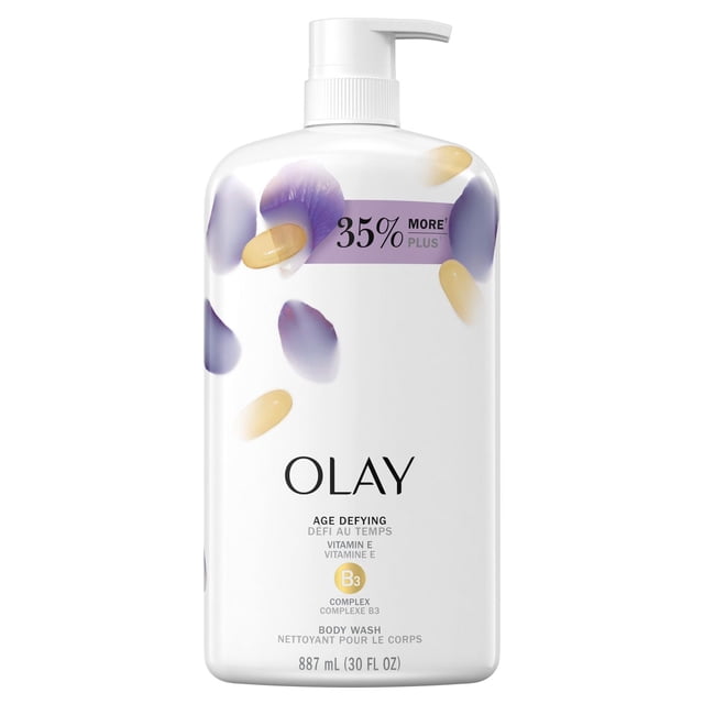 Olay Age Defying Body Wash with Vitamin E in a white 887 mL (30 fl oz) pump bottle featuring purple flower petals and yellow vitamin capsules on the label, designed to hydrate and improve skin moisture for healthy-looking skin.