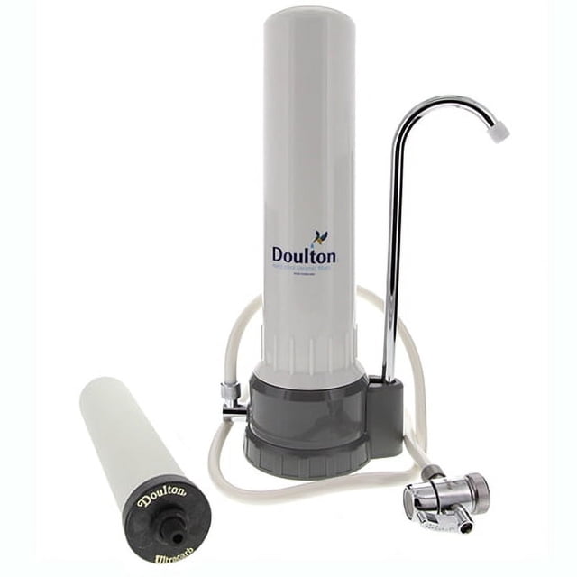 Doulton W9331032 UltraCarb Countertop Water Filter System featuring a white cylindrical housing with a chrome faucet and diverter valve, alongside a cleanable UltraCarb ceramic filter cartridge. Designed for four-stage filtration to reduce contaminants like lead, iron, and bacteria while improving water taste. Compact and easy to install on kitchen countertops.