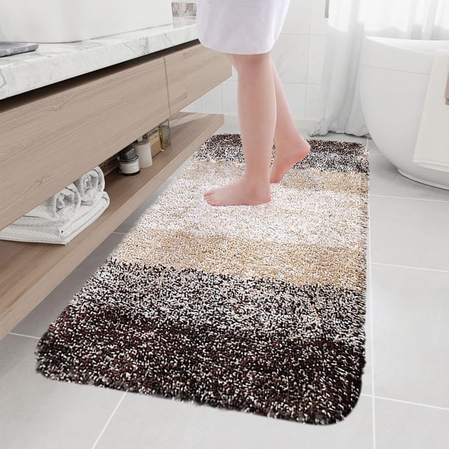 Ihhxbz Big Deals Items Living Room Bedroom Flocking Carpet Plushes Rug Bathroom Absorbent Non Slip Mats Kitchen Foot Mats Machine Wash Bathroom Rugs for Bedroom Bath Tub and Shower. A khaki polyester bath mat measuring 15.7x31.4 inches is displayed in a modern bathroom. The rug features a soft microfiber texture with a striped design in brown, beige, and white tones. Positioned near a sink and bathtub, it emphasizes its non-slip rubber backing, high water absorbency, and machine washable durability. Ideal for bathrooms, kitchens, and laundry rooms.