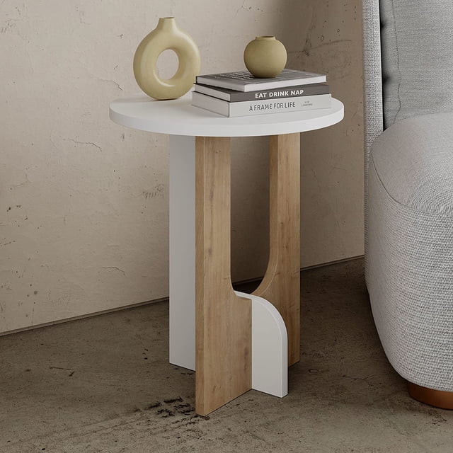 JV Home Luna Table d'Appoint Ronde, une Table de Bout Moderne avec Rangement, avec Dessus Blanc et Pattes Brun Pâle. la Table a une surface Ronde et une Tablette Inférieure, Idéale pour Servir de Petite Table de Nuit dans les Salons Ou les Chambres. Fabriquée en Bois Manufacturé avec un Revêtement en Mélamine durable, Elle Mesure 15,8 Pouces de Diamètre et 47 cm de Hauteur. la Table Est Présentée dans un Décor Minimaliste à Côté d'Un sofa Gris, avec des Objets Décoratifs et des Livres Placés sur le Dessus.