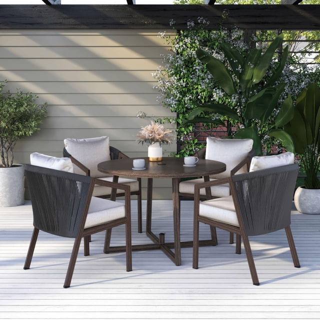 Better Homes & Gardens Laval 5-Piece Steel Outdoor Patio Dining Set with Cushions in brown, featuring a round steel tabletop with hand-painted woodgrain finish and four handwoven resin wicker chairs with curved backs and beige UV- and fade-resistant cushions, set on a light wood deck with potted plants and beige siding wall, ideal for outdoor dining and casual gatherings.