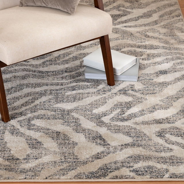 Pescara Tapis Tissé Charbon et Ivoire sous une Chaise beige Rembourrée avec Pattes en Bois, Présentant un Motif d'Impression Animale Texturé dans des Tons Charbon et Ivoire avec une pile de Polypropylène durable et Profil Bas, Idéal pour Ajouter une Touche Moderne aux Espaces de Vie et Adapté aux Zones Très Passantes, Montré avec des Livres Empilés sur le Tapis.