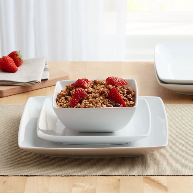 Better Homes & Gardens Loden Square White Dinnerware Set, 12-Pieces showing a square white porcelain bowl filled with granola and strawberries, stacked on matching square salad and dinner plates on a wooden table with a beige placemat and folded napkins, microwave and dishwasher safe, oven safe to 450°F, suitable for everyday dining and serving.