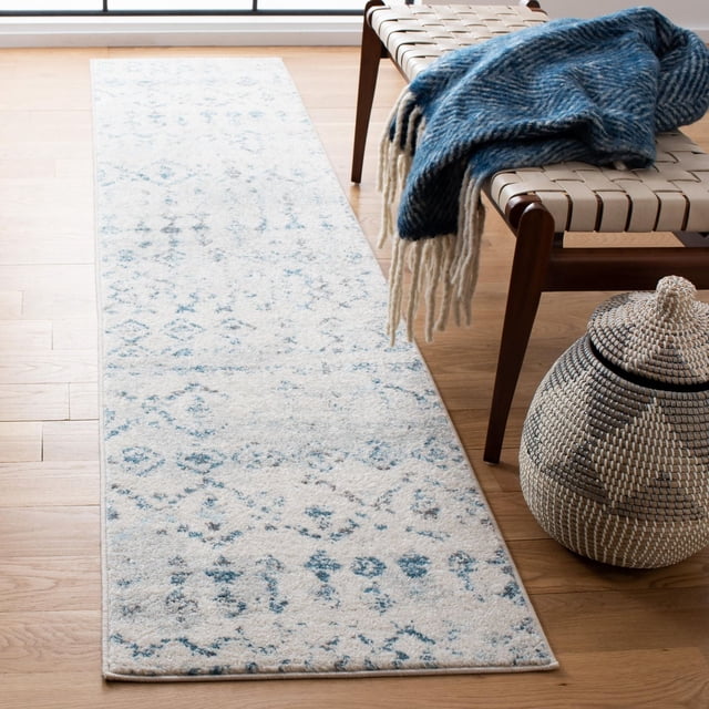 SAFAVIEH Tulum Herbert Distressed Southwestern Area Rug in soft blue and cream tones with a rustic southwestern pattern, displayed as a narrow runner on light hardwood flooring beside a woven bench with a blue fringed throw and a woven basket, suitable for adding cozy, boho-chic character to hallways or entryways.