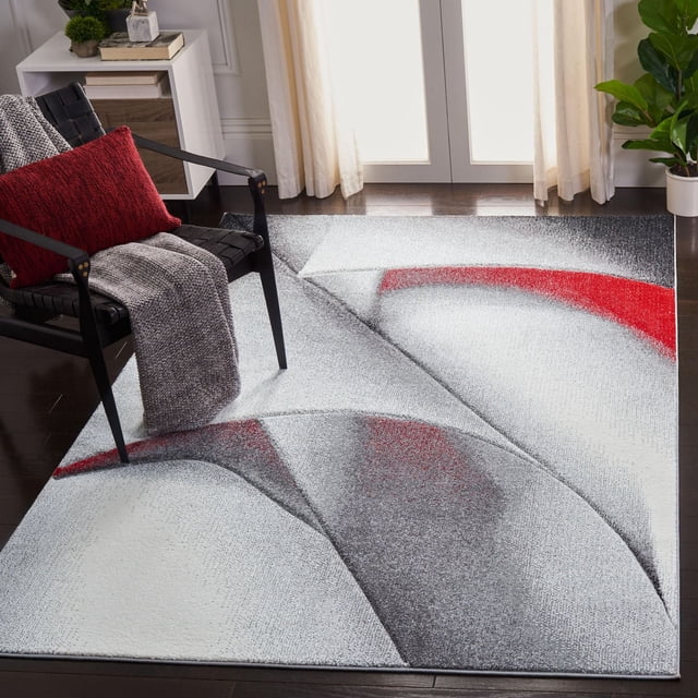 Safavieh Hollywood Salome Abstract Area Rug with mid-century modern geometric abstract design in grey, white, and red, placed on dark hardwood floor beside a black woven armchair with red pillow and grey throw, suitable for accenting contemporary living spaces.