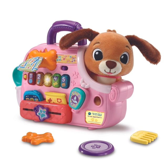 VTech Cutie Paws Puppy Carrier™ With Plush Puppy - French Version is a pink interactive toddler toy carrier with a purple handle and a brown plush puppy inside. It features numbered buttons teaching numbers, colors, shapes, and pet care phrases, plus role-play accessories like a comb, treats, and water bottle, designed for ages 12-36 months to encourage early learning and responsible pet care.
