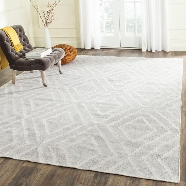 Safavieh Kilim Lorcan Tapis à Losanges Géométriques, Tapis d'Accent à Tissage Plat Présentant un Motif de Losanges Neutre à Légèreté Subtile, Posé sur un Plancher de Bois dans une Pièce Éclatante avec une Chaise Capitonnée Grise avec un Jeté Jaune, un pouf Tricoté Brun et un vase Blanc avec des branches Près de Portes-Fenêtres en Verre.