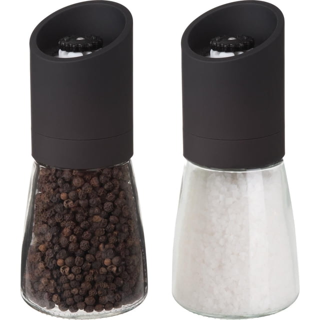 Trudeau 6" Oslo Pepper Mill and Salt Mill set with clear glass bodies and matte black tops featuring rust-proof ceramic grinders positioned on top for mess-free seasoning, filled with whole black peppercorns and coarse white salt, also suitable for precise spice grinding in cooking.