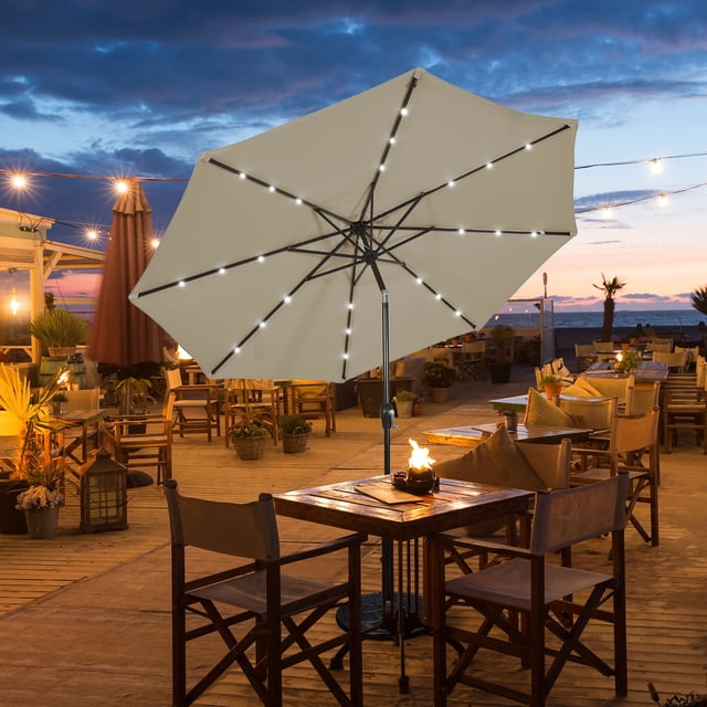 Gymax Parasol de Marché pour Table de Patio de 10 Pi pour Cour et Extérieur avec Lumières DEL Solaires Couleur Beige, Doté d'Un Auvent en polyester de 10 Pieds Soutenu par un Poteau en Fer Enduit de Poudre de 1,5 Po et 8 Nervures Robustes. le Parasol Comprend 24 Lumières DEL à Énergie Solaire Intégrées, Réparties Uniformément avec 3 Lumières par Nervures, Créant une ambiance Chaleureuse pour une Utilisation en Soirée. l'Auvent a une Conception Ventilée pour Améliorer la circulation de l'Air et la Résistance au Vent, et un Mécanisme d'Inclinaison à Bouton-Poussoir
