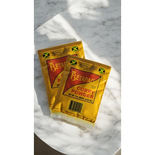 BetaPac Jamaican Curry Powder Twin Pack (2 x 110g) displayed on a white marble surface. The bright yellow packaging features the BetaPac logo, Jamaican flag, and product details, emphasizing its authentic Caribbean spice blend of turmeric, coriander, cumin, and pimento. Ideal for curries, stews, and marinades.