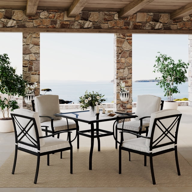 Mainstays Montclair Ensemble de Salle à Manger d'Extérieur 5 Pcs avec Coussins, Gris Pâle avec une table à Manger Carrée avec Dessus en Verre Trempé Fumé et Quatre Chaises Rembourrées avec Cadres en Acier Noir Résistants à la Rouille, Ensemble sur un Tapis d'Extérieur beige sous une pergola en Bois avec des Piliers en Pierre Surplombant une Vue Côtière, Idéal pour les Repas en Plein Air et les Rassemblements Décontractés.