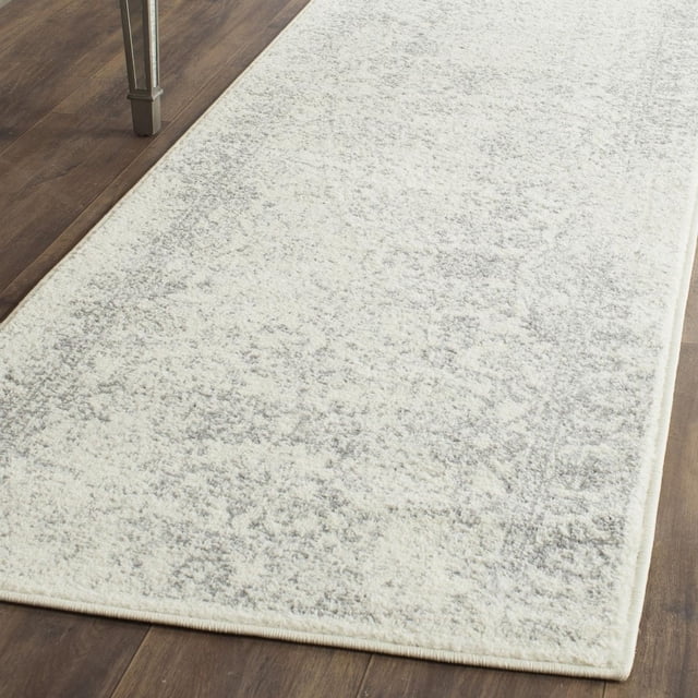 SAFAVIEH Adirondack Wyatt Traditional Area Rug with a light neutral base and subtle gray over-dye pattern, made of durable polypropylene yarns, power loomed in Turkey, displayed on dark hardwood floor under a table leg, suitable for rustic lodge style home accents.
