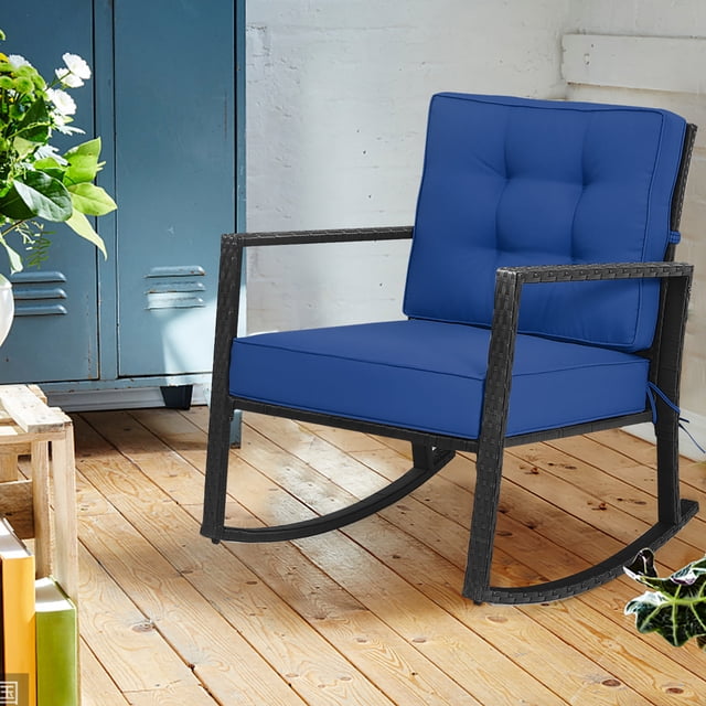 Costway Patio Rattan Rocker Chair Outdoor Glider Rocking Chair with navy cushions, featuring a black PE rattan frame and sturdy metal construction. The chair includes a thick 5-inch seat cushion and a 3.5-inch back cushion, both secured with strings to prevent movement. Designed with an angled backrest, slightly downward handrails, and anti-slip pads at the base for safety. Suitable for indoor and outdoor spaces such as patios, gardens, or living rooms. Dimensions: 26.5 inches long, 36 inches wide, and 33 inches high.