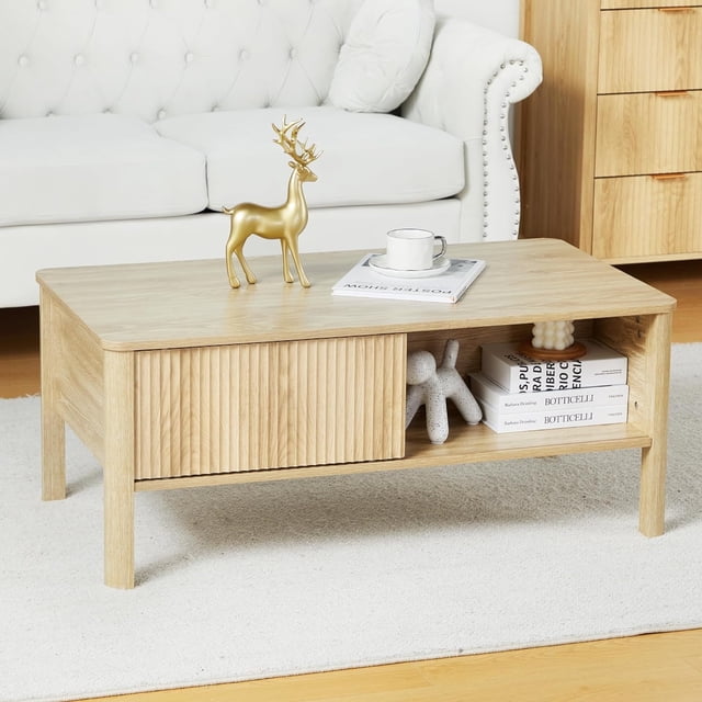 Wirrytor Table Basse Carrée Cannelée de Style Mi-Siècle avec Double Tablette de Rangement, Dotée d'Une Finition en Bois Naturel et d'Une Porte à Panneau Ondulé Coulissante. la Table Comprend Quatre Compartiments de Rangement, Idéale pour Organiser des Livres, des Télécommandes et de la Déco. Fabriquée à Partir de Panneaux MDF Robustes avec des Pieds en Bois Massif, Elle Présente des Bords Courbés Lisses pour la Sécurité et une Capacité de Charge jusqu'à 220 Livres. Exposée dans un Décor de Salon avec un sofa Blanc et des Articles Décoratifs.
