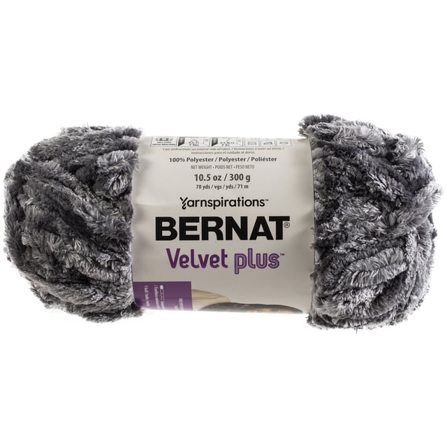 Bernat Velvet Plus yarn in grey, a super bulky #6 polyester yarn weighing 10.5 oz (300 g) and measuring 78 yards (71 m), shown in a close-up front view with a plush, velvety texture and a label displaying brand and care details, ideal for quick knitting and crafting projects.
