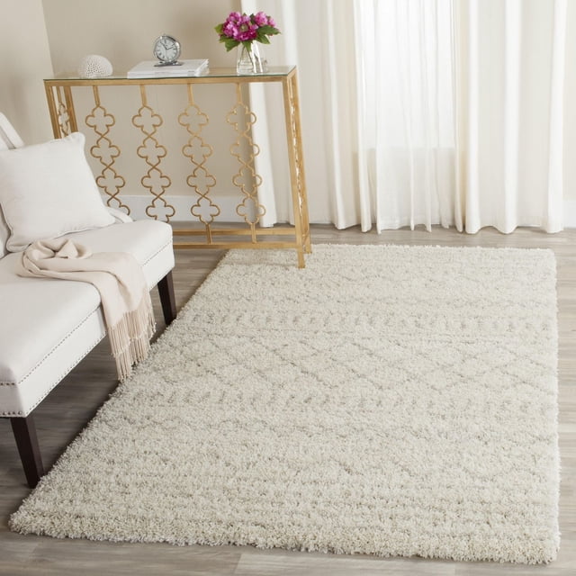 Safavieh Arizona Teagan Geometric Stripes Shag Area Rug in cream with 1.25-inch medium pile and geometric tribal patterns, placed on light wood flooring in a bright room with a white upholstered bench and gold metal console table, suitable for adding warmth and texture to living areas.