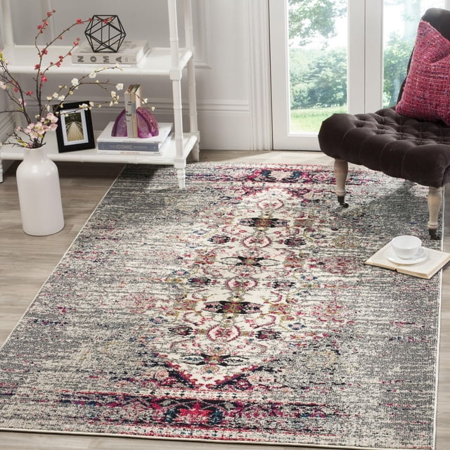 Safavieh Monaco Elsdon Abstract Area Rug with a central ornate cream and pink pattern accented by dark blue on a textured gray polypropylene surface, placed on light wood flooring near a white shelving unit and a dark tufted chair with a pink cushion, suitable for adding Bohemian-chic flair to home decor.