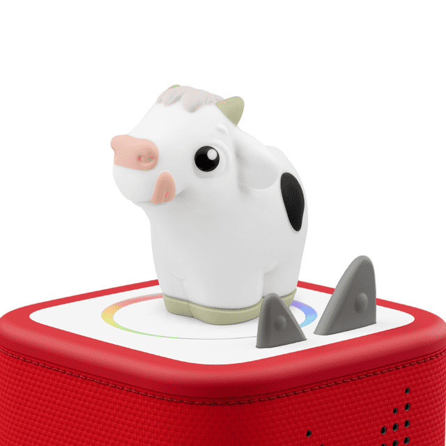 tonies My First Tonies: Cow showing a white and black spotted cow figurine with a pink snout and beige horns on a red square base with a white top featuring a colorful circular design, an educational electronic toy supporting early learning and language development for children aged 1 and up.