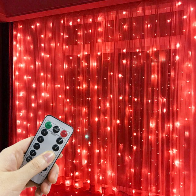 1 Pack LED Curtain Lights with USB 8 Modes Remote Control, featuring 300 red LEDs arranged in a 3x3 meter grid. The lights are displayed hanging against a window with sheer curtains, creating a warm and festive ambiance. A hand holding the included remote control is visible in the foreground, showcasing the control options for brightness and lighting modes. Suitable for home, wall, window, fairy garden parties, weddings, and Christmas decorations.