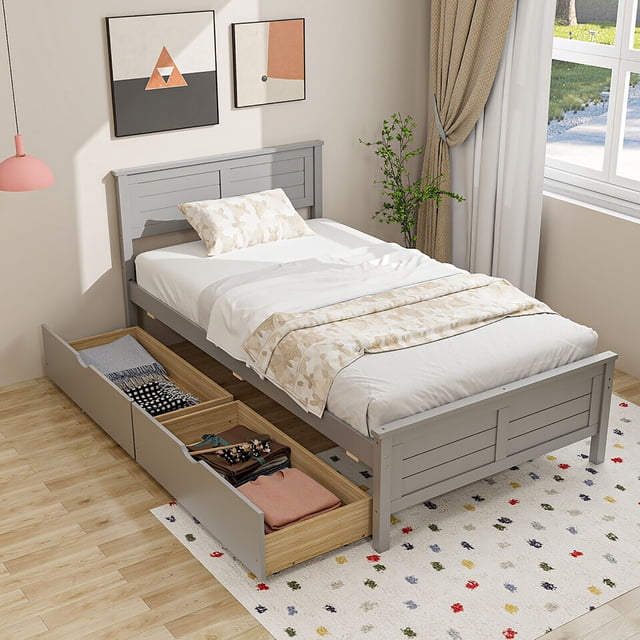 Gymax Twin Size Wooden Bed Frame with 2 storage drawers and under-bed storage in gray. This platform bed features a solid wood headboard and footboard with a slatted design, ensuring durability and a modern aesthetic. Two large pull-out drawers with cut-out handles and smooth wheels are positioned under the bed, offering ample space for clothes and other belongings. The drawers can be used on either side of the bed and include stoppers to prevent over-sliding. Ideal for compact storage solutions, the bed is shown in a bright bedroom setting with natural light, wooden flooring, and decorative accents.
