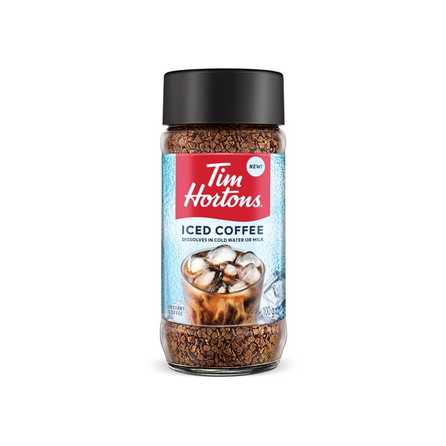 Tim Hortons Instant Iced Coffee in a clear glass jar with a black lid, containing brown granules made from 100% Colombian Arabica beans. The label features the Tim Hortons logo on red, states it dissolves quickly in cold water or milk, and shows an image of iced coffee with ice cubes. Suitable for making refreshing iced coffee drinks.
