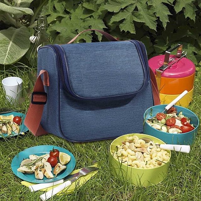 Cooler Lunch Bag in navy color with a large capacity design, featuring a front flap and adjustable shoulder strap. The bag is displayed outdoors on grass, surrounded by picnic items such as colorful bowls of food, cutlery, and a tiffin box. Suitable for men, women, kids, and teachers, this insulated lunch bag is ideal for work, travel, picnics, and outdoor activities.