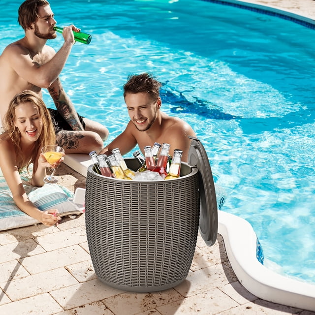 Costway 9.5 Gallon 4-in-1 Patio Rattan Cool Bar Cocktail Table Side Table in brown, displayed by a pool. This versatile outdoor furniture piece functions as an ice bucket, side table, stool, and storage box. The rattan-style design enhances patio aesthetics, and the open lid reveals beverages chilled with ice. Features include a 9.5-gallon capacity, side handles for portability, and a drainage plug for easy maintenance.