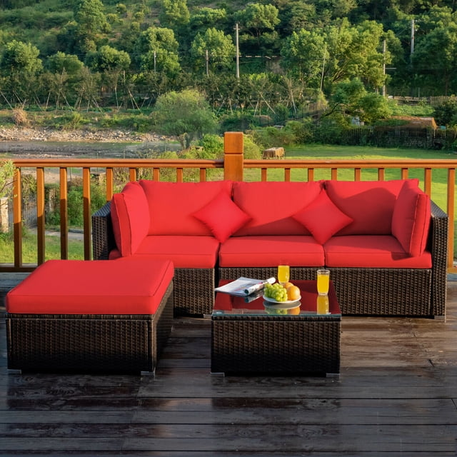 Gymax Ensemble de Canapé Sectionnel en Rotin 5 Pcs, Ensemble de Mobilier de Patio avec Coussins et Oreillers Rouges, Présentant un design Modulaire avec Deux Canapés d'Angle, un Canapé Sans Accoudoirs, un ottoman et une table Basse avec Dessus en Verre Trempé. l'Ensemble Est Fait de Rotin PE durable et d'Un Cadre en Acier Enduit de Poudre, Convient à l'Utilisation Extérieure. les Coussins Ont une Épaisseur de 4 Pouces et Sont Recouverts d'Un Tissu polyester Imperméable. Exposé sur un Patio en Bois avec un Paysage Vert Pittoresque en Arrière-Plan.