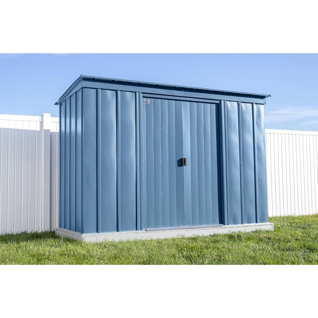 Arrow Classic Steel Storage Shed, 10x4, Blue Grey, front view showing vertical galvanized steel panels with a pent roof to prevent water pooling, pad-lockable sliding doors on a concrete base with grass and white fence background, ideal for storing garden tools and equipment.