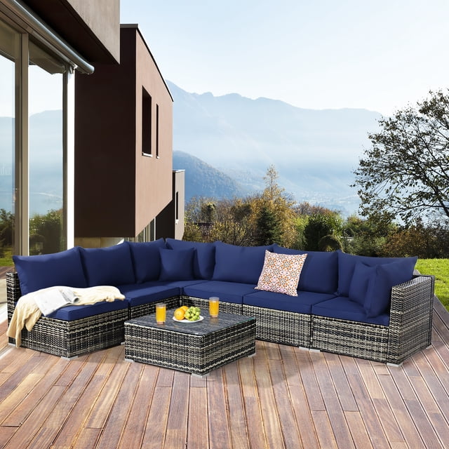 Costway 7PCS Patio Rattan Furniture Set Sectional Sofa Garden Navy Cushion arranged on a wooden deck with a scenic mountain view. This outdoor sectional features mix-gray rattan, navy cushions, a tempered glass coffee table, and pillows for added comfort, ideal for patios or gardens.
