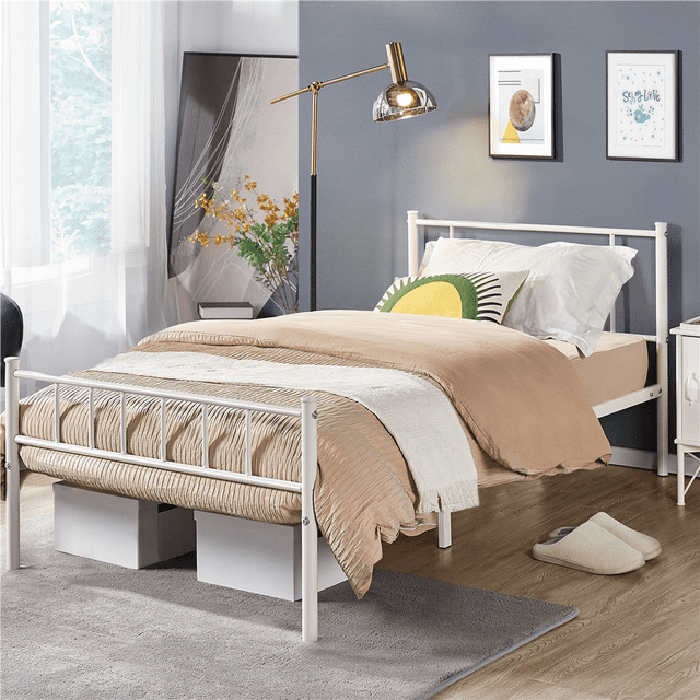 Fullfurnique Metal Platform Bed Frame with Headboard and Footboard, twin size in white, shown with beige bedding and white pillows including a green and yellow accent pillow. The metal frame features vertical spindle design, sturdy slats, and 13 inches of under-bed storage with white boxes. The bedroom has a gray wall with framed art, brass floor lamp, sheer curtains, wood flooring, gray rug, and slippers. Ideal for compact spaces like dorms or apartments.