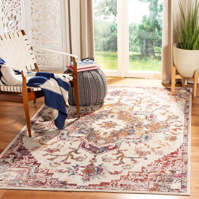 SAFAVIEH Crystal Tapis Floral Debra à Poils Courts et Motifs de Médaillons Floraux Complexes en Rouges, Bleus et Dorés Atténués sur Fond Crème, Exposé sur Plancher de Bois dans une Pièce Ensoleillée avec une Chaise Tissée Drapée d'Un Jeté Bleu et beige, un pouf Tricoté Gris Surmonté de Livres et de Lunettes, et une Grande Plante en Pot, Idéal pour Rehausser la Déco du Salon Ou de la Salle à Manger.