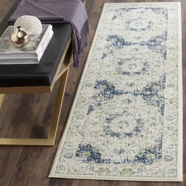 SAFAVIEH Evoke Teale Traditional Area Rug, a durable polypropylene frieze runner with a soft texture and faded floral medallion pattern in blue, cream, and beige, shown on a hardwood floor beside a black cushioned bench with gold legs and a folded purple throw, suitable for adding style and comfort to narrow spaces.
