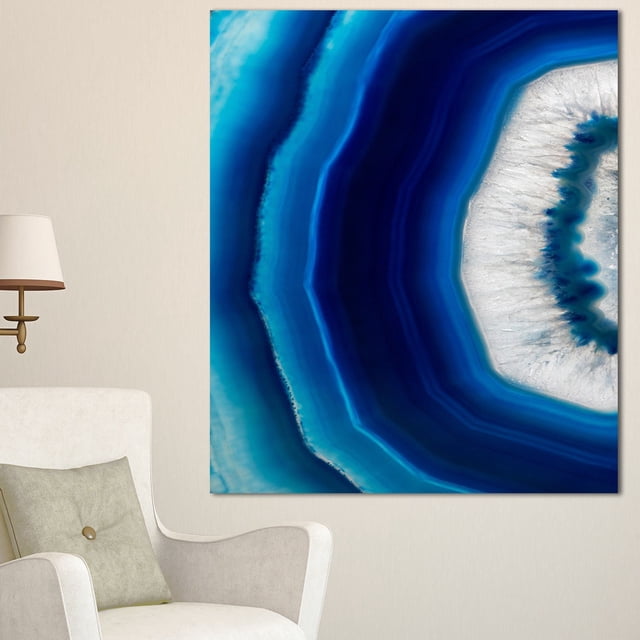 Design Art Blue Agate Crystal Abstract Digital Art Canvas Print showing detailed blue and white agate crystal layers in a gallery wrapped canvas on a 1-inch wood subframe, ready to hang on a beige wall above a white armchair with a green cushion and a brass wall lamp, suitable for enhancing home décor.