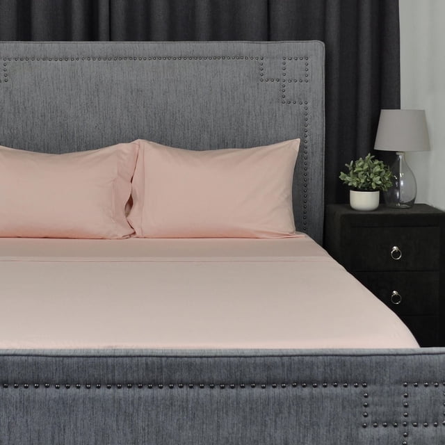 100% Cotton White Sheet Set with 400 thread count on a bed with grey upholstered headboard featuring nailhead trim, including deep pocket fitted sheet, flat sheet, and two pillowcases in soft pink, set in a bedroom with dark curtains and a black nightstand with lamp and plant, ideal for comfortable, durable, and easy-care bedding.