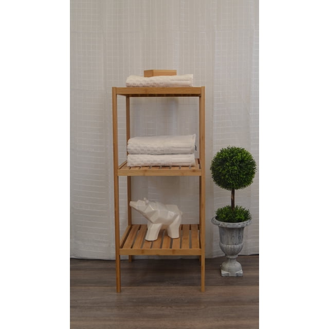 3 Tier Bathroom Tower Shelf Free Standing Bamboo by Nola Home & Furniture. This freestanding bamboo shelf features three spacious tiers with slatted surfaces, ideal for storing towels, toiletries, or decorative items. The natural bamboo finish complements various bathroom decors, creating a spa-like atmosphere. The shelf measures 31 inches in height, 13.4 inches in width, and 13 inches in depth, with an 11-inch distance between shelves. Displayed in a bathroom setting with towels, a decorative ceramic figure, and a potted plant.