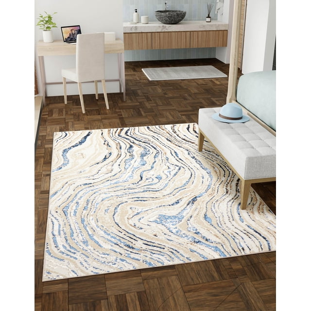 ECARPET Mercan Contemporary/Modern Area Rug with fluid marble and sand-inspired beige, blue, and cream patterns, placed on dark parquet flooring in a bedroom featuring a light gray bench with a blue hat, wooden desk with beige chair, and floating vanity with stone vessel sink.