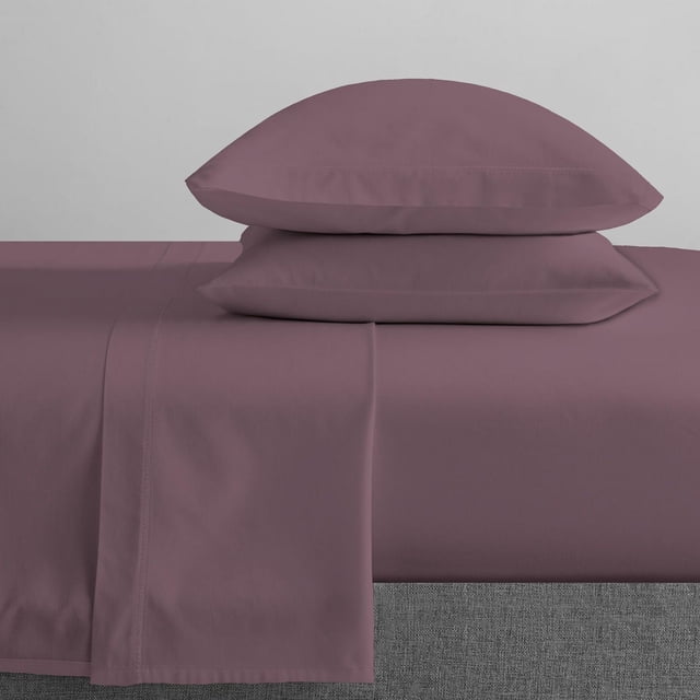 Johnson Home 500 Thread Count Certified Organic Cotton Sheet Sets in muted plum, displaying a fitted sheet, flat sheet, and two pillowcases stacked on a bed with a grey upholstered base, highlighting the smooth, breathable organic cotton fabric that offers durability and year-round comfort.