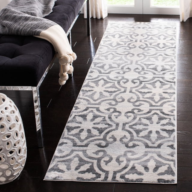 Safavieh Isabella Eliza Tapis Géométrique Floral en Gris Doux et Blanc avec un Motif Floral Géométrique Répétitif, Fils Synthétiques Tissés Mécaniquement en Poil de Coupe Moyenne, Placé sur un Plancher de Bois Franc Foncé à Côté d'Un Banc Noir avec des Pattes Chromées et un Jeté Gris, Près de Portes en Verre avec des Rideaux Blancs, Idéal pour une Utilisation Classique Ou Décontractée comme Tapis Coureur.